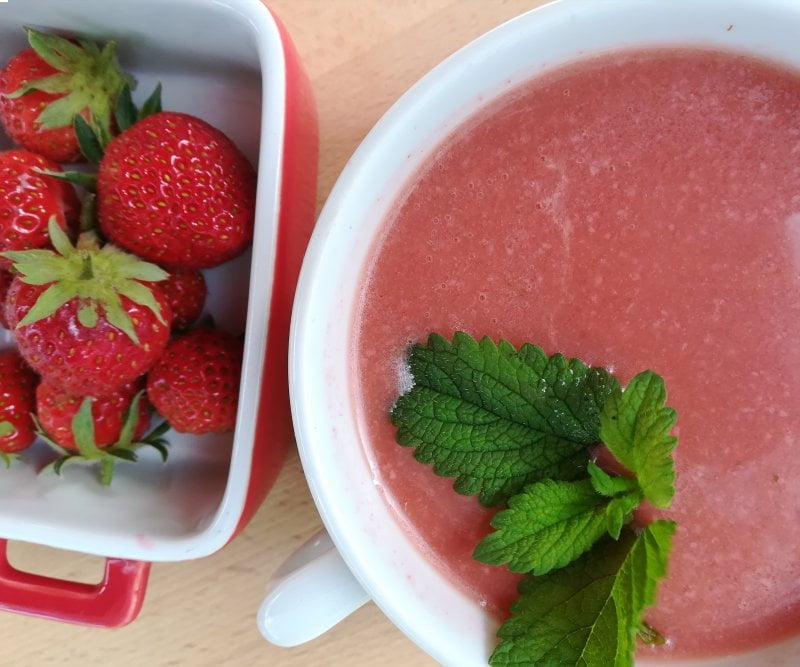 desde arriba una taza de gazpacho conuna ramita de hierbabuena y al lado un cuenquito con fresas