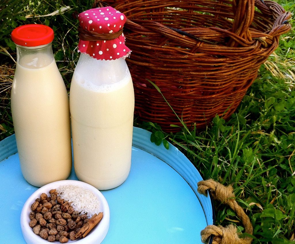 como concervar leches vegetales dos botellas de vidrio con leche dentro en una bandeja . Al lado unas semillas y una cesta.