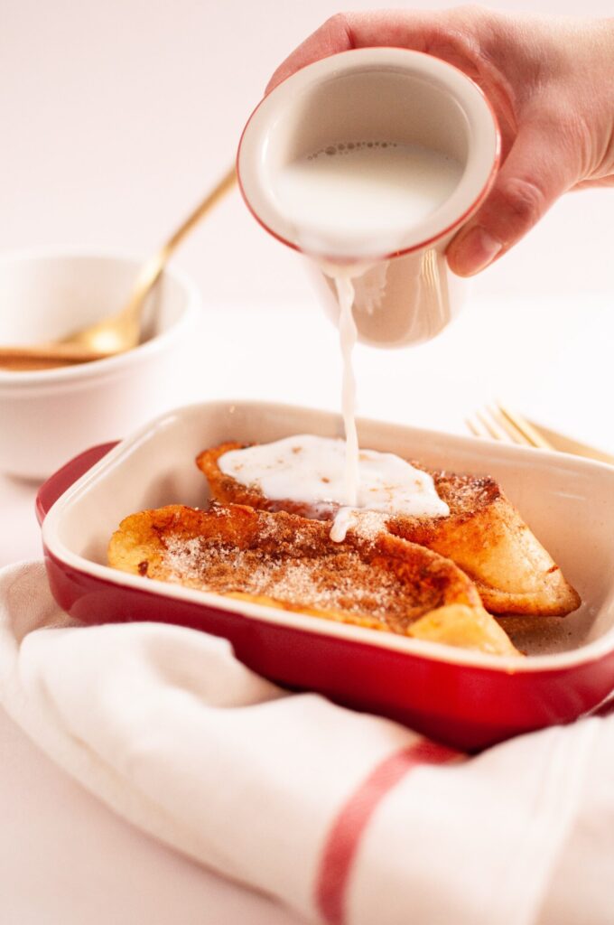 receta de torrijas veganas sin gluten bandeja de cocina con dos torras y una mano con una jarrita de leche vertiendo la leche sobre las torradas